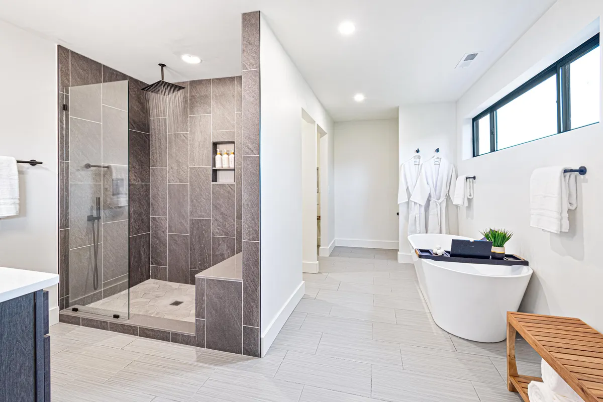 A pristine bathroom featuring a spacious walk-in shower, a freestanding bathtub, a well-designed vanity area, and plush bathrobes. The space is bright and calming, with a focus on both functionality and relaxation.