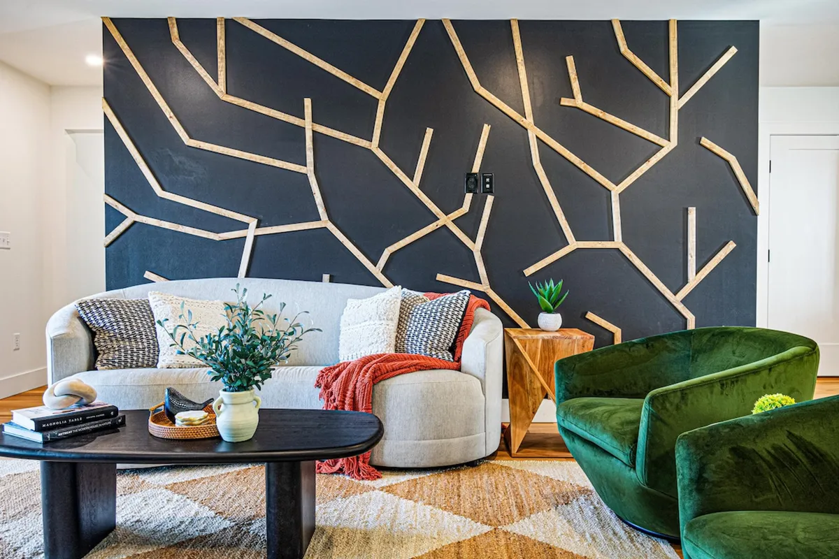 A cozy interior corner furnished with green accent chairs, a geometric wood wall, and a coffee table. The arrangement creates a welcoming spot for reading, meditation, or relaxed conversation.