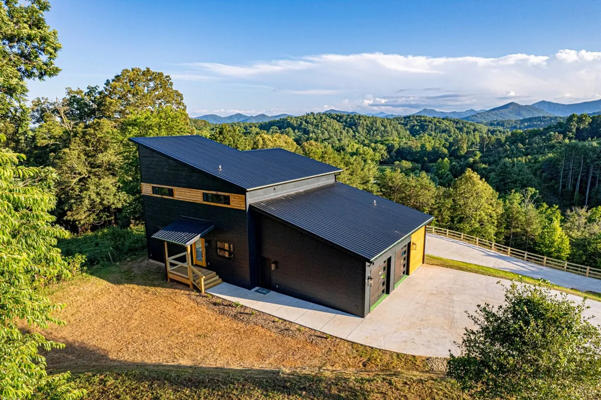 A wide exterior shot of a modern home nestled in the landscape, with the driveway leading up to the house and panoramic mountain views stretching behind. The serene setting invites outdoor exploration and frames the home as a gateway to nearby trails and adventures.