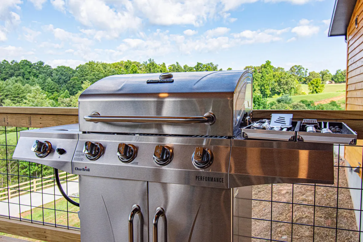 An outdoor scene featuring a stainless steel grill set against a scenic landscape. The setting includes grilling accessories and an inviting space for gathering, suggesting opportunities for outdoor dining and group barbecues.