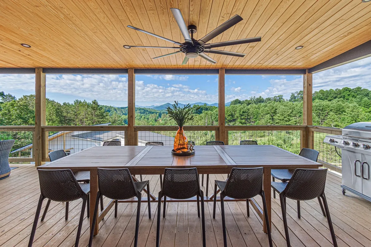 The photo features a large outdoor dining table set on a spacious deck, overlooking the majestic mountains. There's also an outdoor grill and stylish decorative touches, providing a space for both quiet solo work or lively gatherings with friends and family.