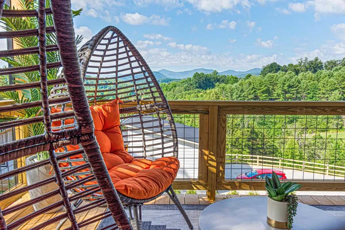 A cozy hanging chair set on an outdoor patio, surrounded by lush greenery and offering unobstructed mountain vistas. The tranquil setting is ideal for birdwatching, reading, or simply soaking in the beauty of the Blue Ridge region.