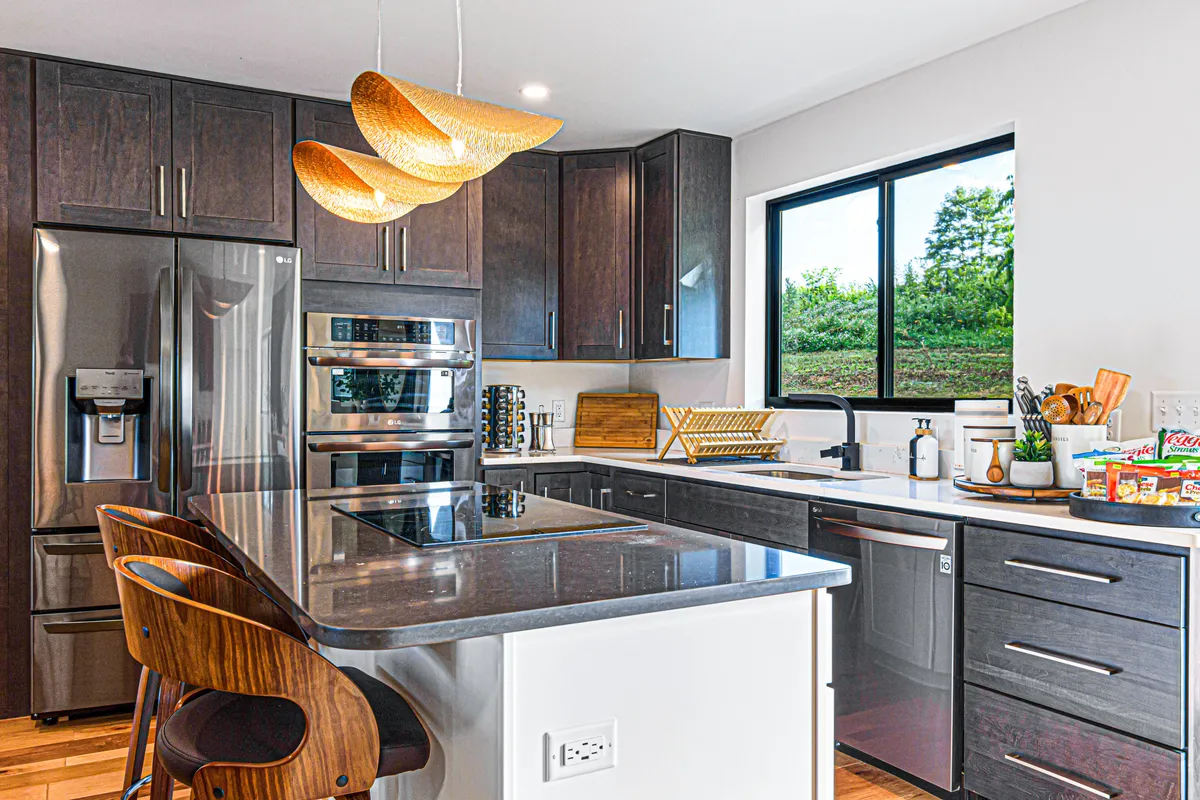 A contemporary kitchen featuring a spacious island countertop, gleaming stainless steel appliances, stylish pendant lighting, and a large window that offers mountain views and floods the space with natural light. The open layout is perfect for cooking, entertaining, and family gatherings, with modern cabinetry and thoughtful design elements making it a chef's dream.