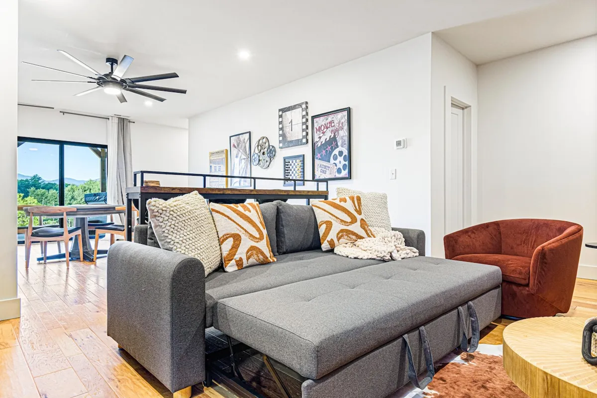 An interior shot of a comfortable living space with a modern sofa, artistic wall decor, a dining table, and large window framing views of the surrounding nature. The overall ambiance is contemporary and inviting, ideal for unwinding or casual work sessions.