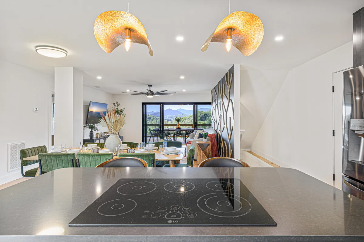 A modern kitchen and dining area with a central island, contemporary lighting, and large windows framing mountain views. Stylish furnishings and high-end finishes abound, creating an ideal setting for cooking, dining, and socializing.